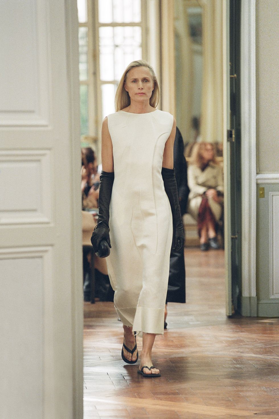 a ﻿model at the row's spring 2023 show wearing flip flops with a white dress and leather opera gloves