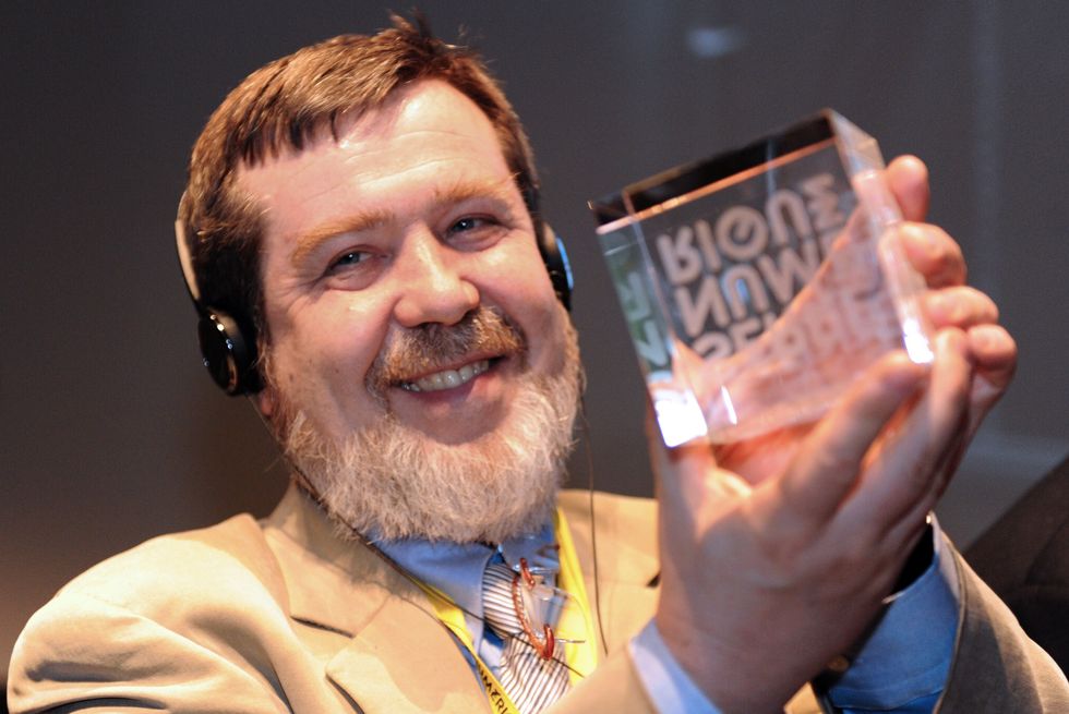 alexey pajitnov﻿, wearing a tan suit and headphones, holds a glass cube trophy and smiles