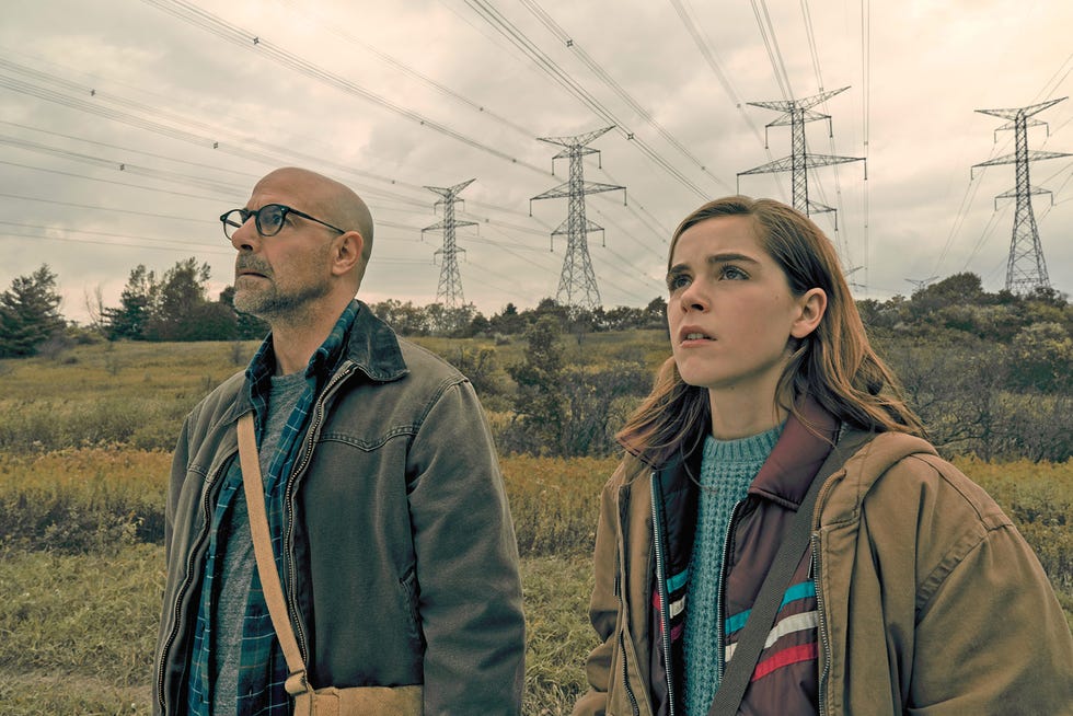 stanley tucci y kiernan shipka miran hacia arriba, abrigados, en medio del campo, en una escena de la película the silence