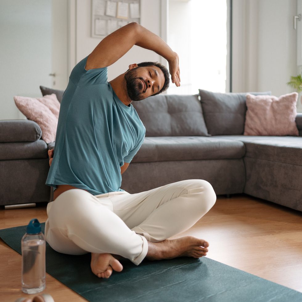 the single man exercising alone at home, stretching his back and arm. young man is happy, relaxed, and content with his life. solo home workout and meditation, morning or evening workout routine.