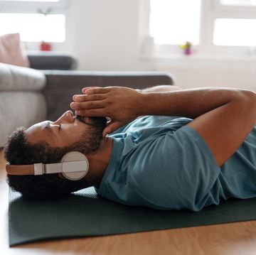 the single man meditating alone at home while listening to meditation music through wireless headphones, doing breathing exercises