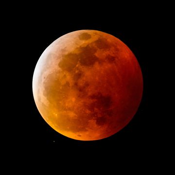a blood moon, or full moon with a reddish shadow due to a total lunar eclipse, in the night sky
