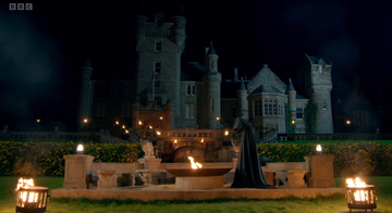 the traitors castle with a fire pit showing one of the cloaked traitors minah