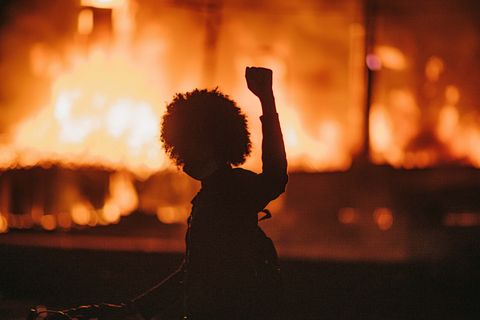 a silhouette of a person holding up their fist with a fire in the background