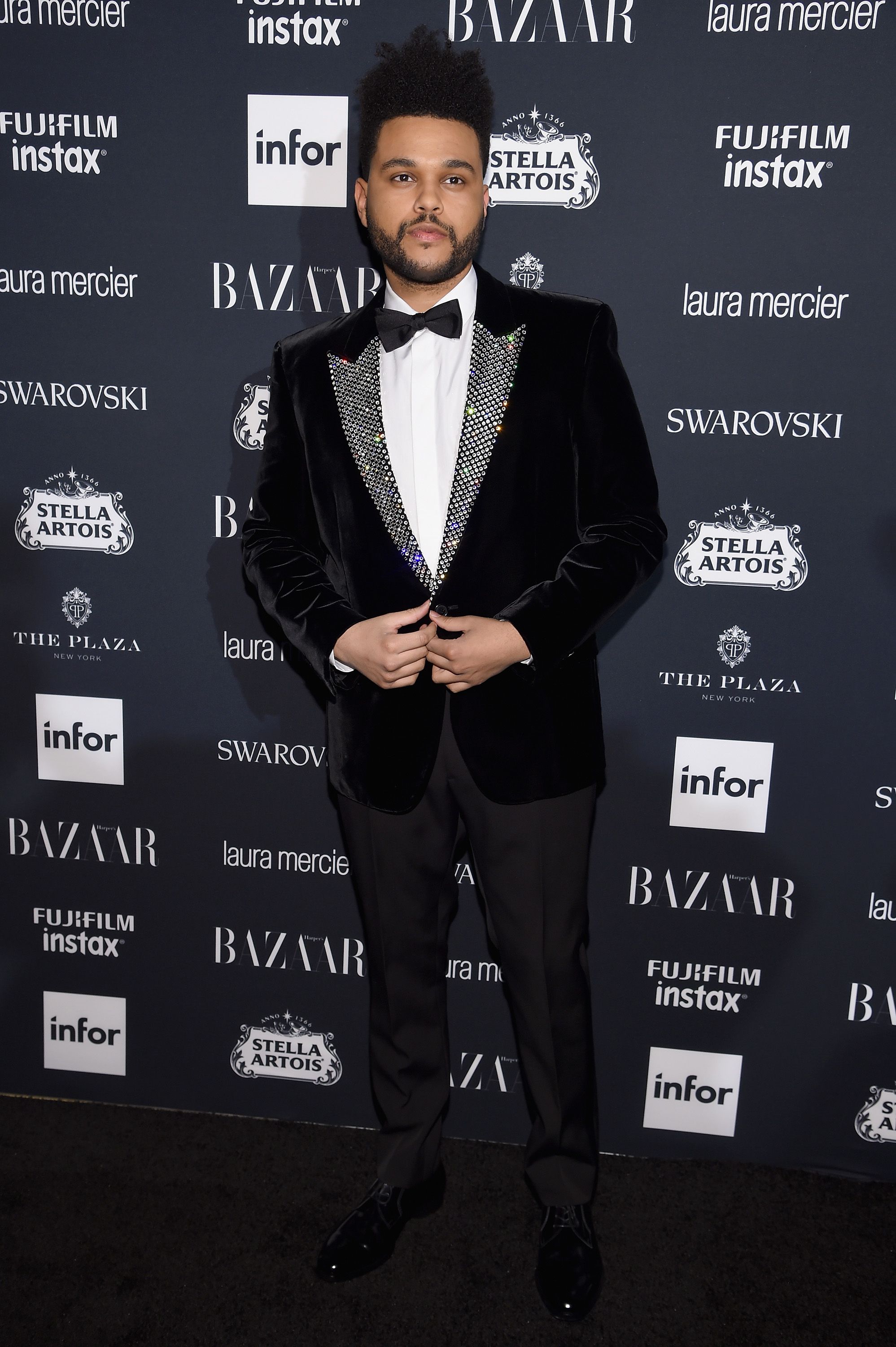 The Weeknd walked the red carpet in a classic Valentino black suit and  bowtie. He added an oversize flower brooch as a final accent – replay254