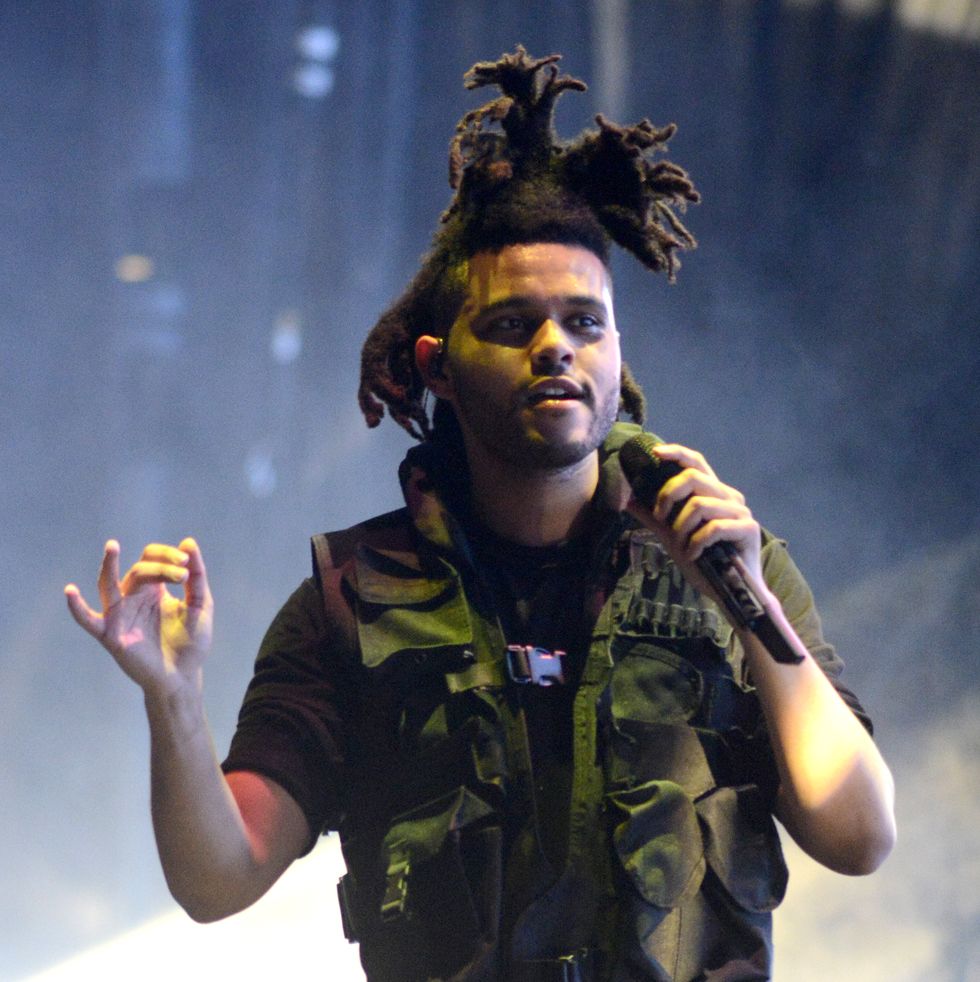 the weeknd sings into a wireless microphone he holds in one hand as he performs in dramatic lighting