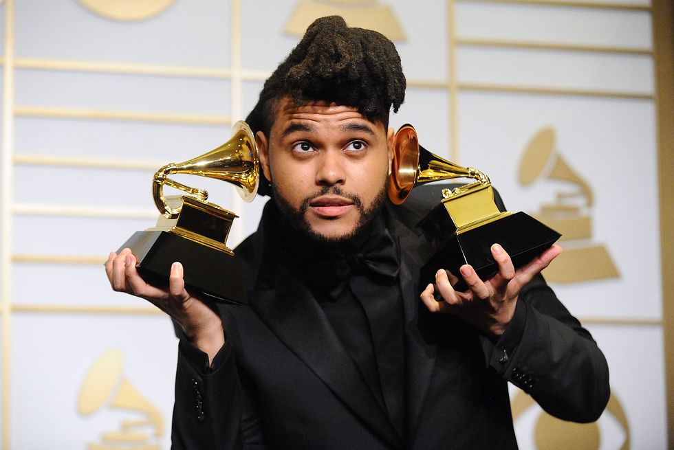 a man in a black suit and shirt holds two grammy trophies up to his face as he looks upward