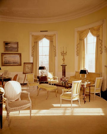 yellow colored room in white house with elegant furniture  two windows  paintings lining the walls  and other glam touches