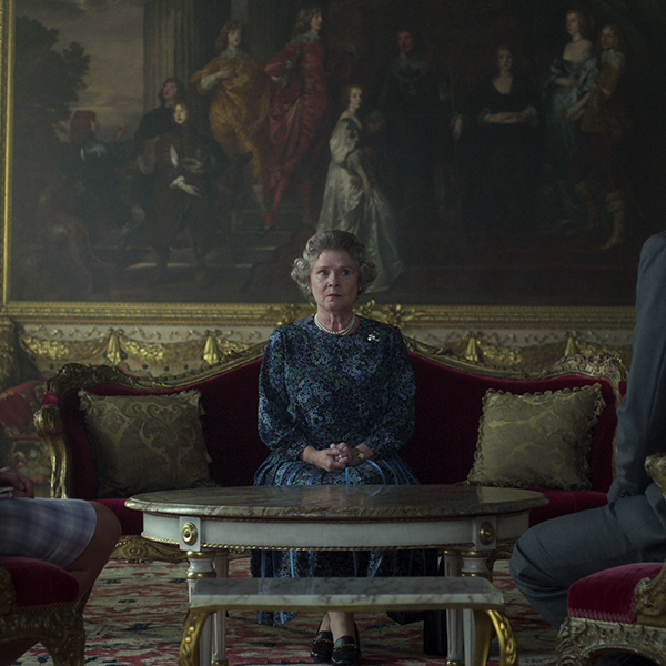 still from the crown showing imelda as the queen sitting on a red ornate couch