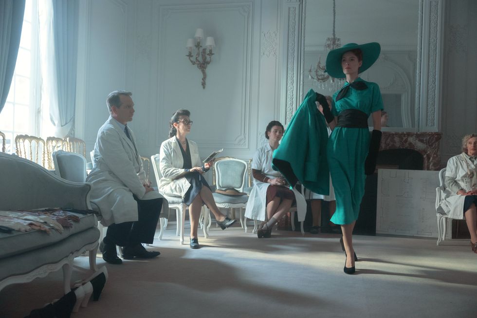 a person in a green dress walking in a room with people sitting in chairs