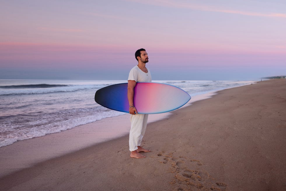 a man holding a surfboard on a beach at sunset