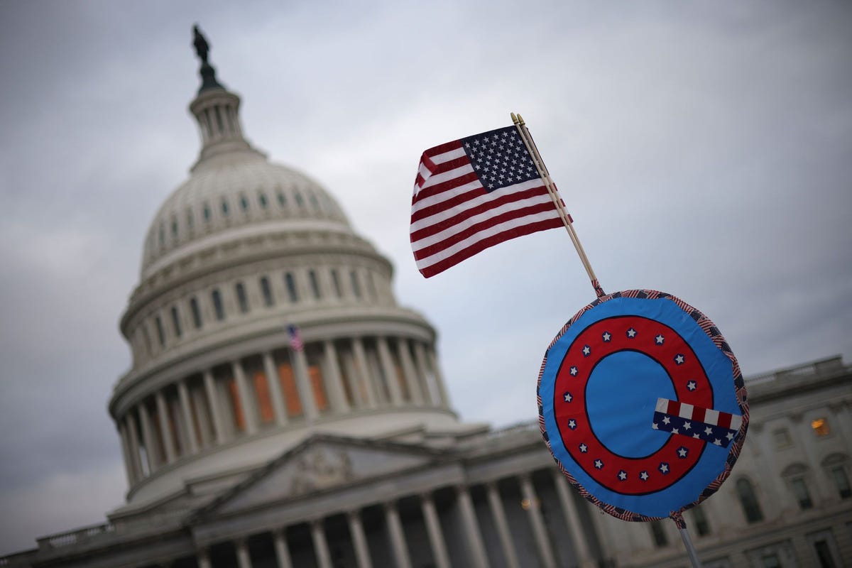 Aanhangers van president Trump hebben een Amerikaanse vlag bevestigt aan een symbool dat staat voor de QAnoncomplottheorie tijdens hun bijeenkomst bij het Amerikaanse Capitool op 6 januari 2021 in Washington