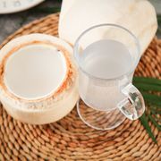 open coconut and a glass of coconut milk on a woven placemat