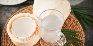 open coconut and a glass of coconut milk on a woven placemat