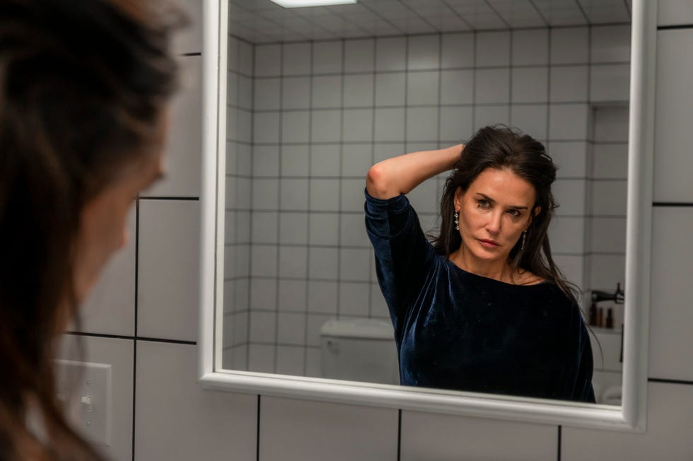 Reflection of a woman adjusting her hair in a bathroom mirror