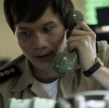 actor hoa xuande holding a cord phone to his left ear with a concerned look on his face in a scene from the sympathizer