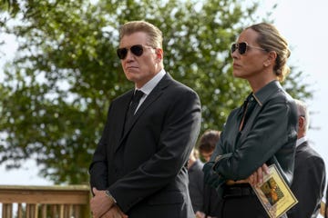 man and woman wearing sunglasses and standing menacingly while at a funeral service