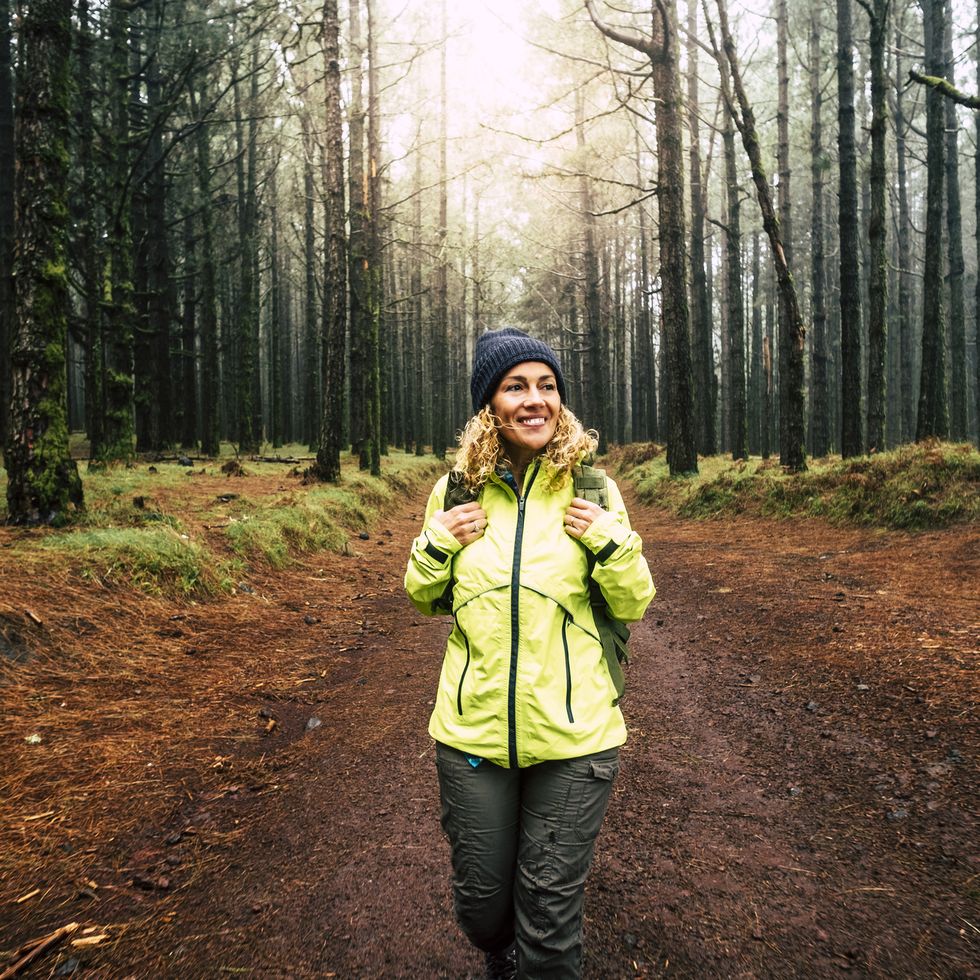happy hiker caucasian woman smile and enjoy the nature walking in a forest with high trees alternative outdoor leisure activity and vacation lifestyle sun in backlight and mist concept