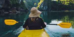 things to do by yourself  woman kayaking in a lake with mountains
