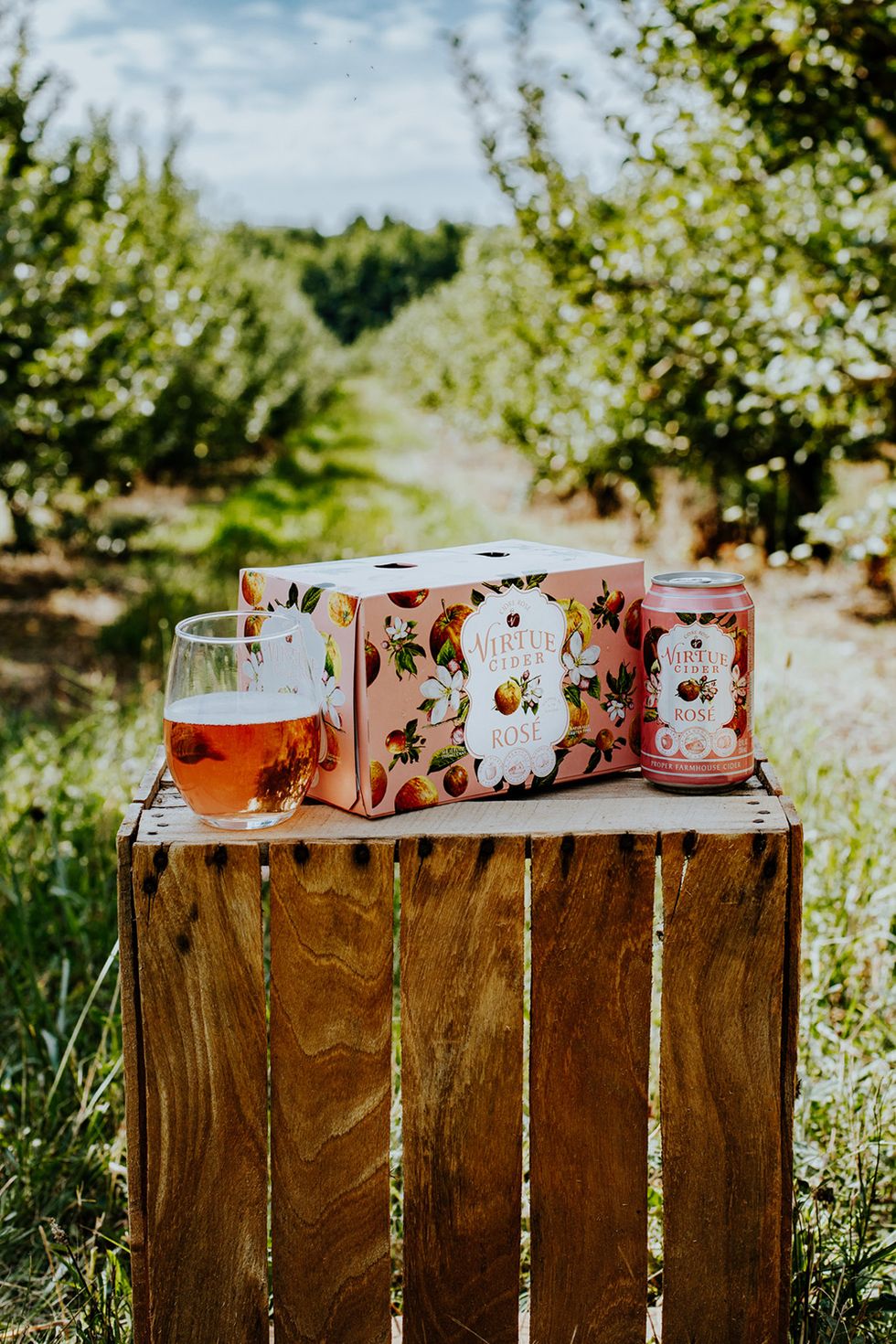 pink virtue cider rose can and box on wooden crate in apple orchard
