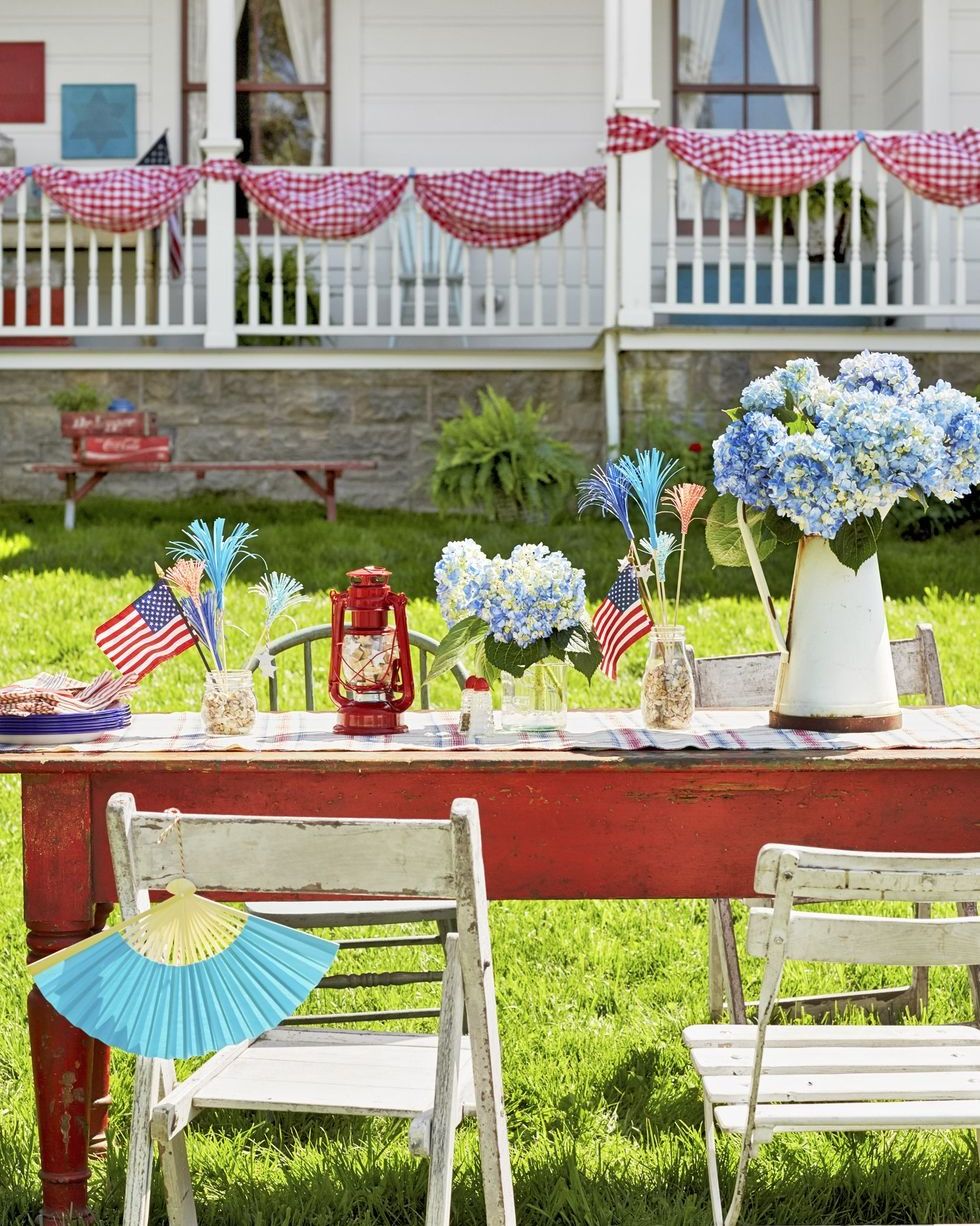 red farm table decorated for 4th of july with vases of blue hydrangeas and red lanterns