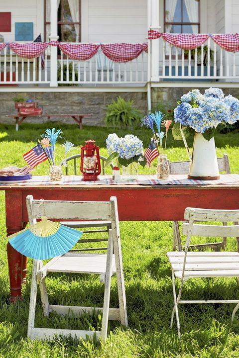 red farm table decorated for 4th of july with vases of blue hydrangeas and red lanterns