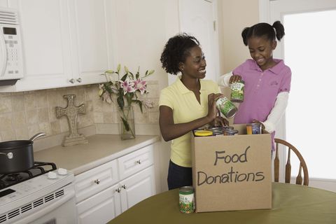 mother and daughter putting canned food in donations box indoors