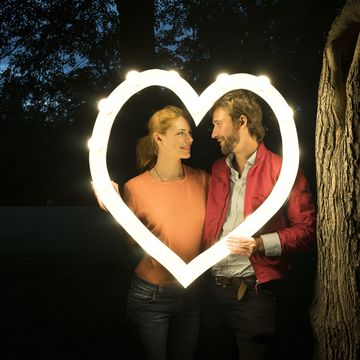 happy couple holding glowing heart next to tree