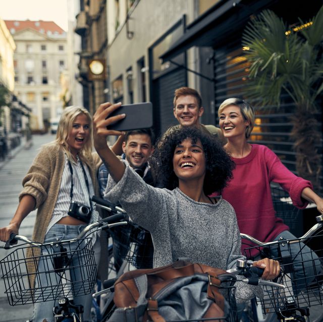5 friends on bicycles with metal baskets in a city pedestrian zone taking selfie