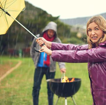 vrouw barbecuet in de regen met paraplu erboven