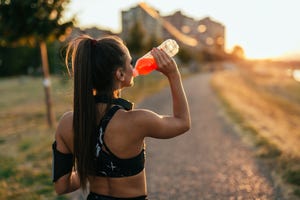 Thirsty woman with headphones drinking sports drink from her bottle