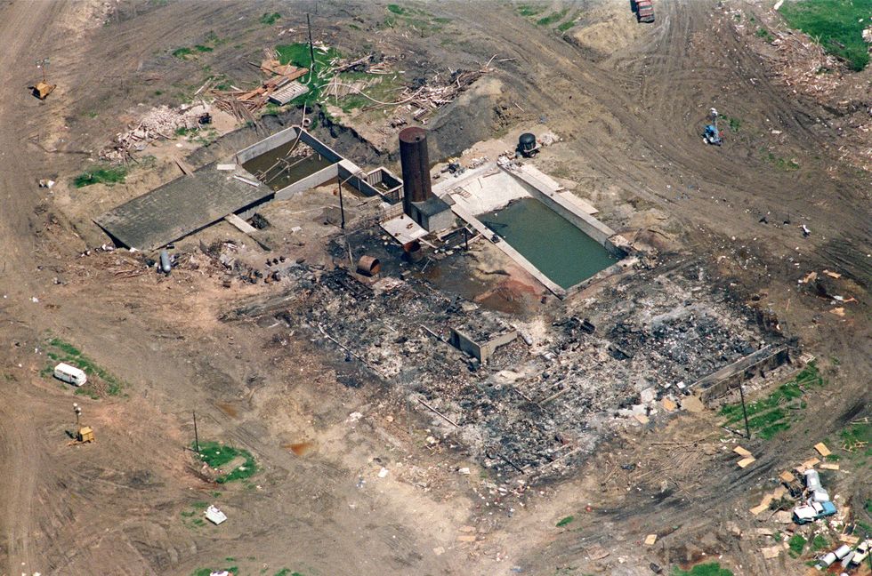 an aerial shot of the burnt remains of a compound, surrounded by dirt roads