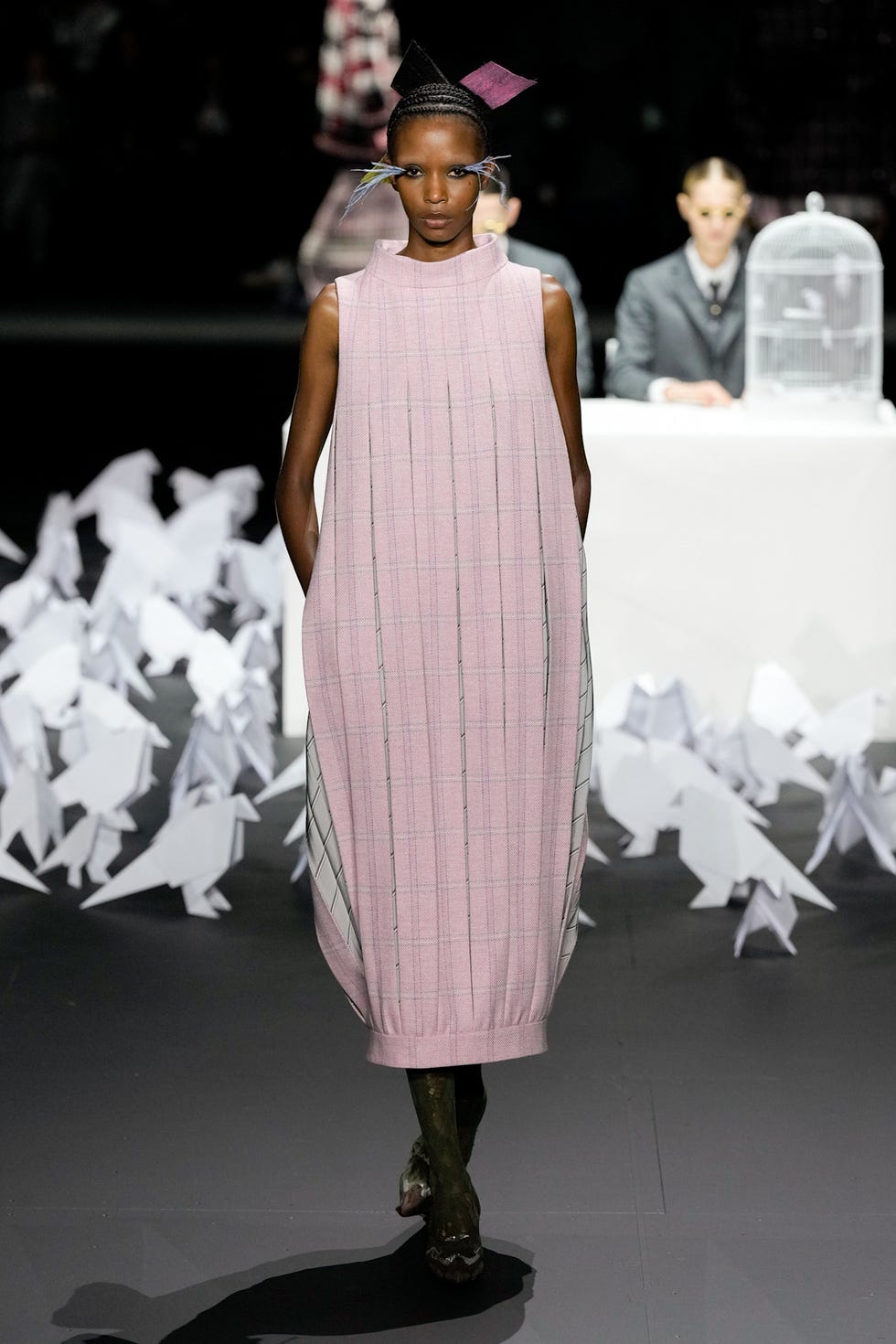 Fashion model showcasing a pink dress in a runway setting with origami figures in the foreground