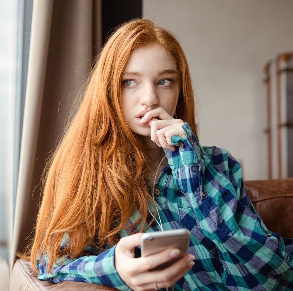 thoughtful unconfident redhead lady listening to music from mobile phone