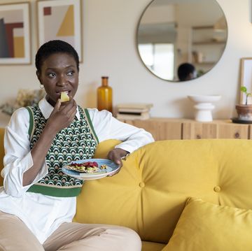 thoughtful woman eating fruits on sofa at home