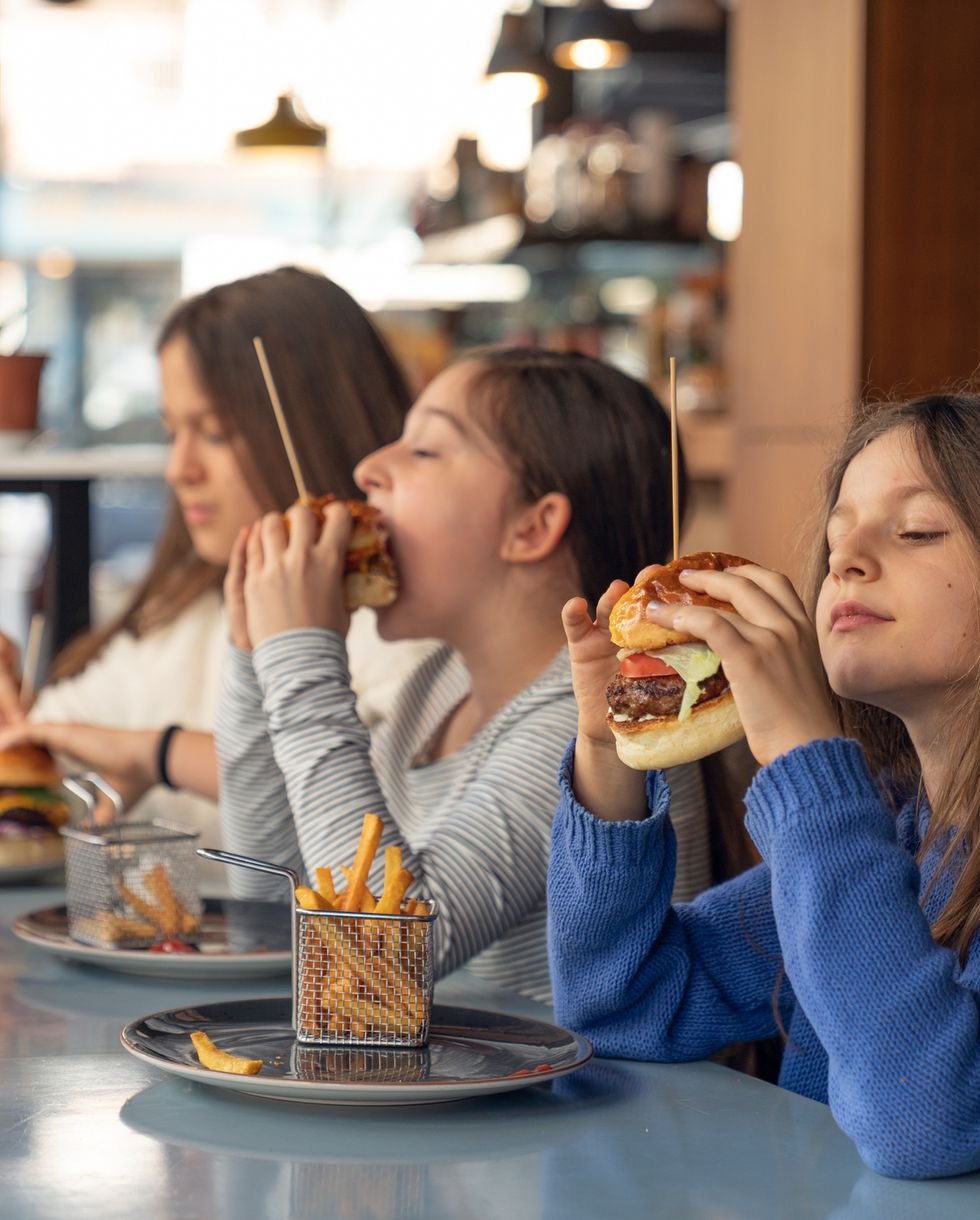three beautiful girls eating hamburgers in fast food restaurant