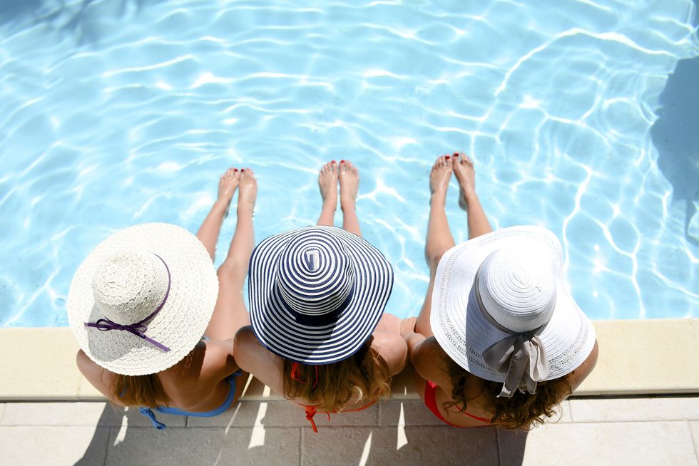three beautiful young woman with swimsuit and sun hat sitting by the poolside of resort swimming pool during summer holiday