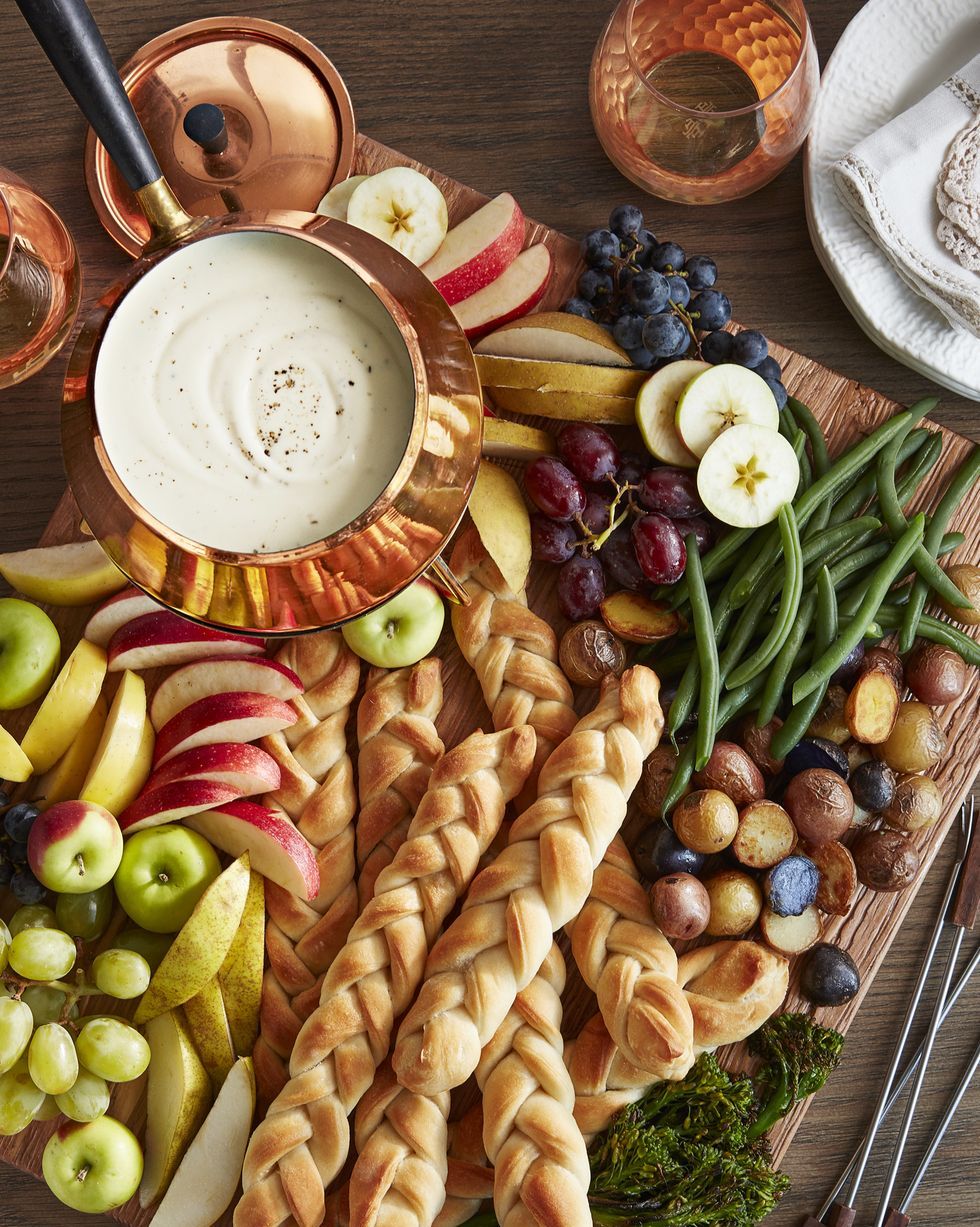 three cheese fondue on a wooden board with various fruits and vegetables for dipping