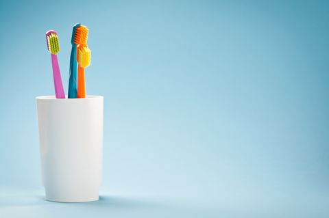 three colourful soft toothbrushes in white mug on blue background
