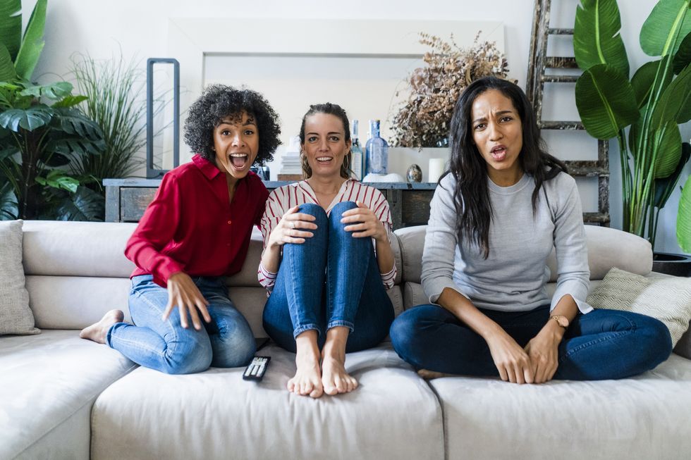 three excited women on couch at home watching tv