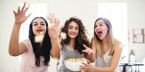 Three female teenager friends eating popcorn at home, having fun.