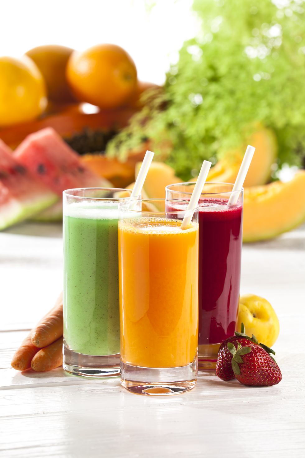 three glasses of fruit juice with fruits in the background