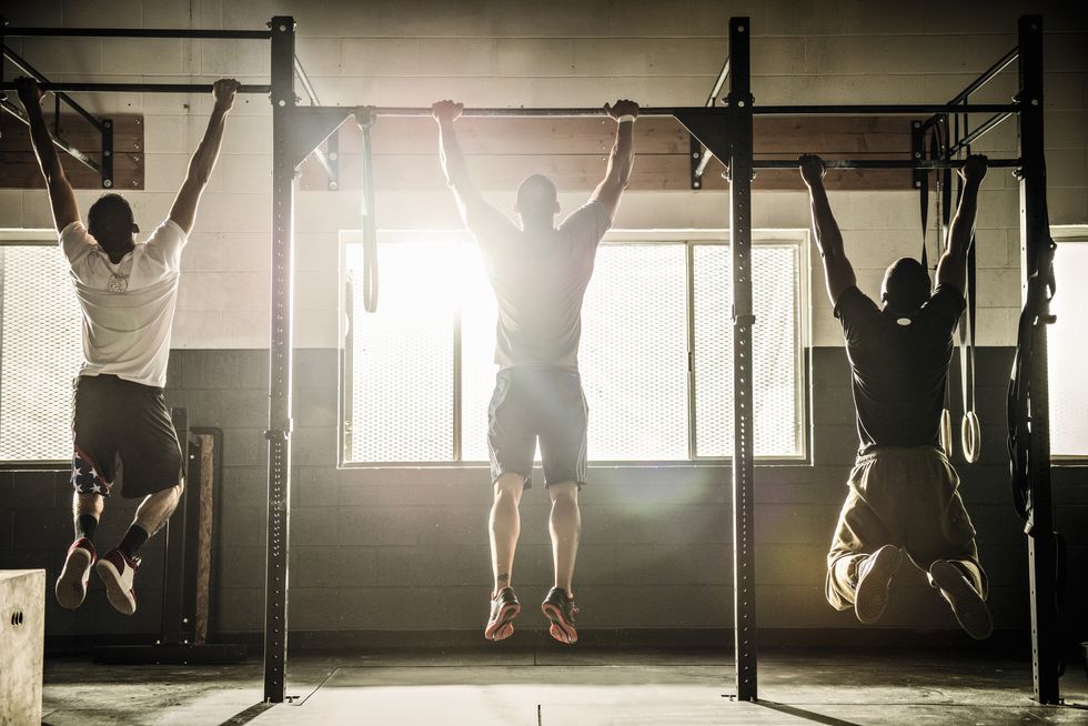 three men doing pull ups on exercise bar in gymnasium