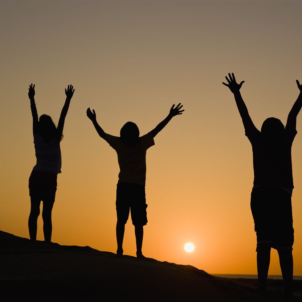 three people enjoying the sunset while raising arms