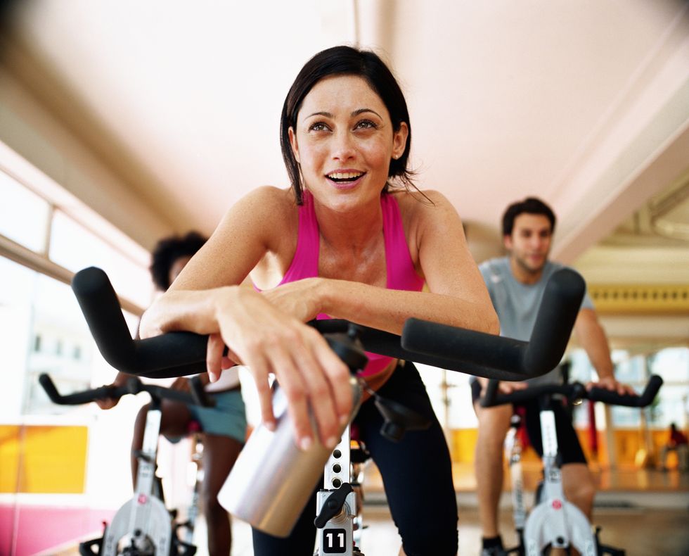 three people sitting on exercising bikes in gym, close up