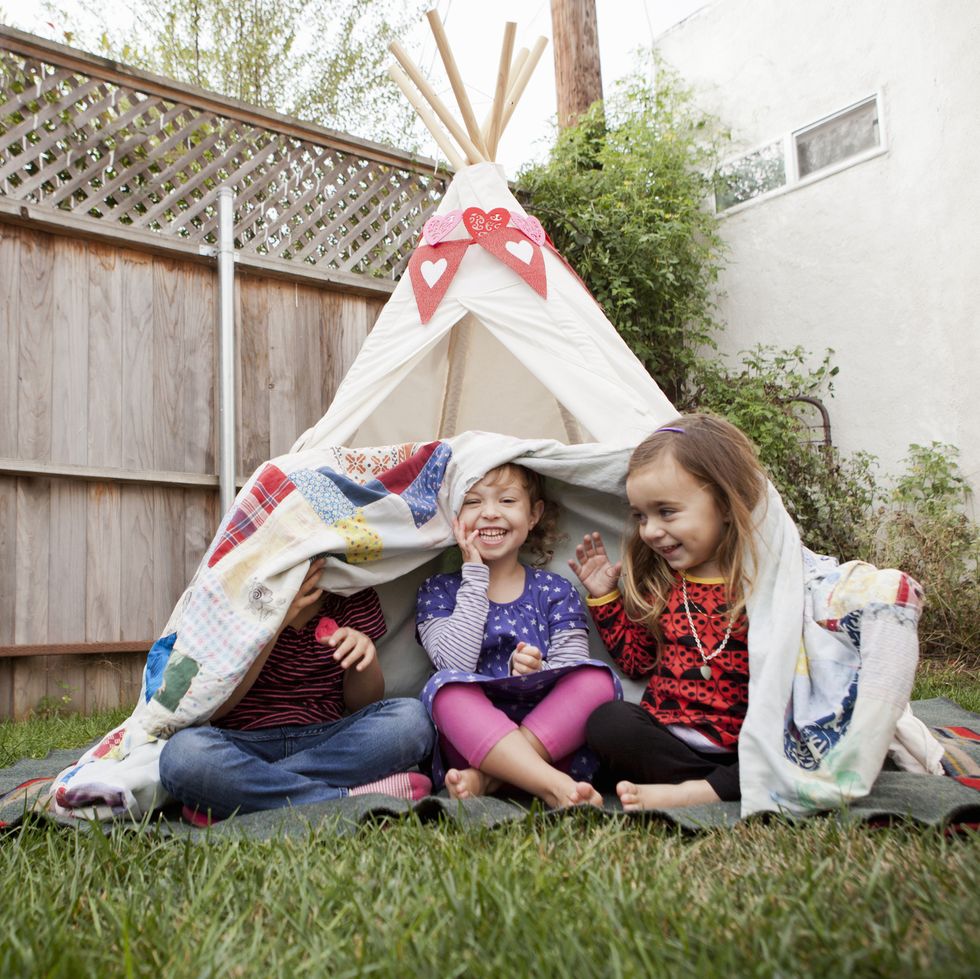 three young girls in garden hiding under blanket