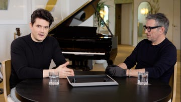 a couple of men sitting at a table with a piano in the background