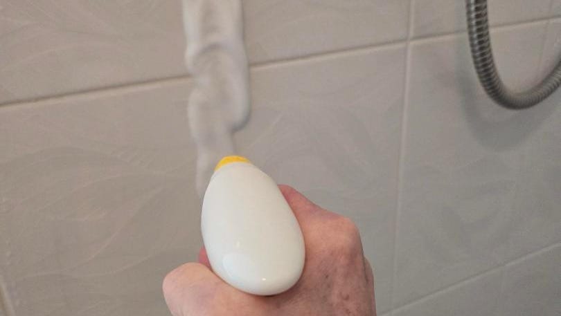 a hand holding a yellow cleaning spray bottle the nozzle is putting foam cleaner on the wall of the shower a woman's hand shown operating the bottle a hand holding a yellow cleaning spray bottle the nozzle is putting foam cleaner on the wall of the shower a woman's hand shown operating the bottle