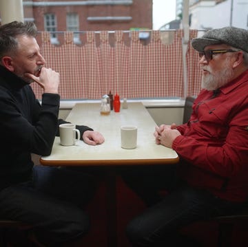 a couple of men sitting at a table with a laptop and a cup of coffee