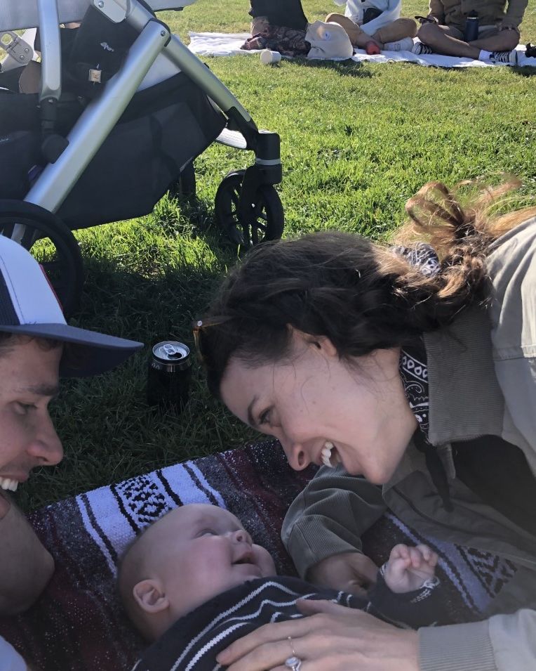 carly leahy and her husband charlie with their baby lying on a blanket in the park